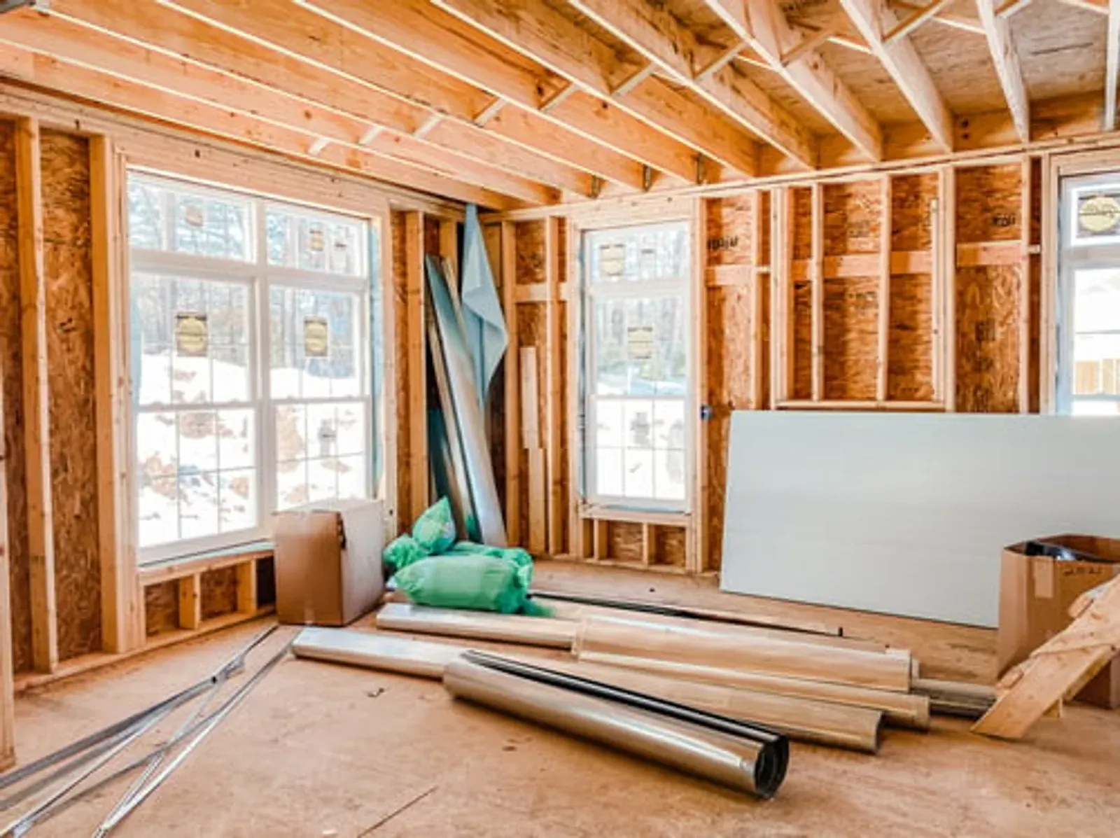 Framed interior of a Big Bear home addition with fresh snow visible through the new windows